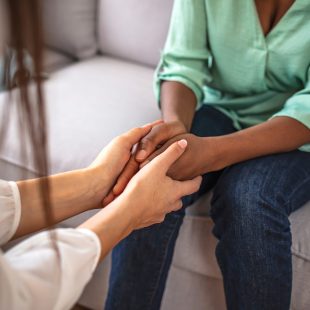Close up African American psychotherapist holding clipboard, touching patient hands, expressing empathy and support at meeting, counselor therapist comforting girl during personal therapy session